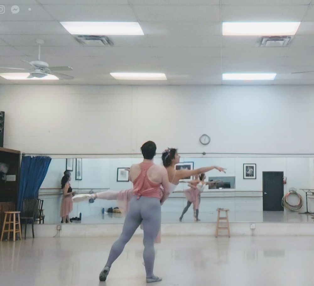 The author and another dancer executing a partnered arabesque, seen from behind, while two other dancers look on.