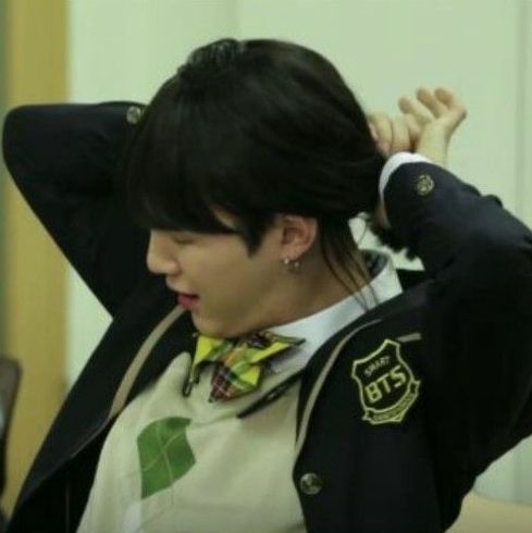Photo sequence of Yoongi (a young man), dressed as Yoonji (a high school girl), tieing up her hair. She is wearing a high school uniform with a yellow and red checkered bow on her collar, a beige vest, and a black blazer.