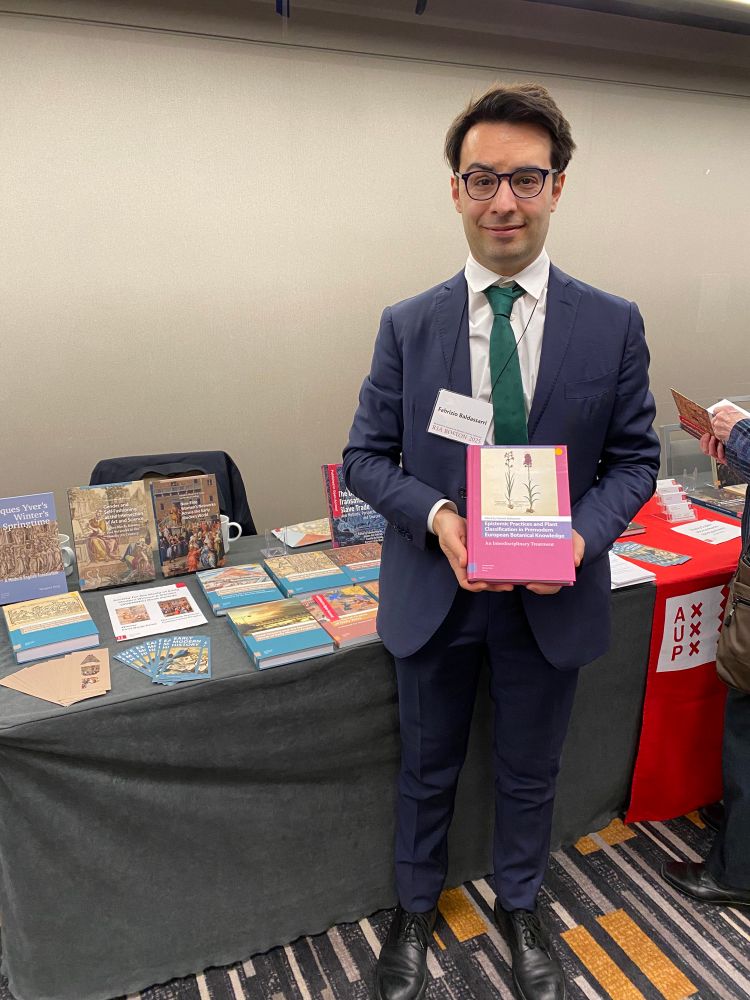 Author holds book in front of book table 