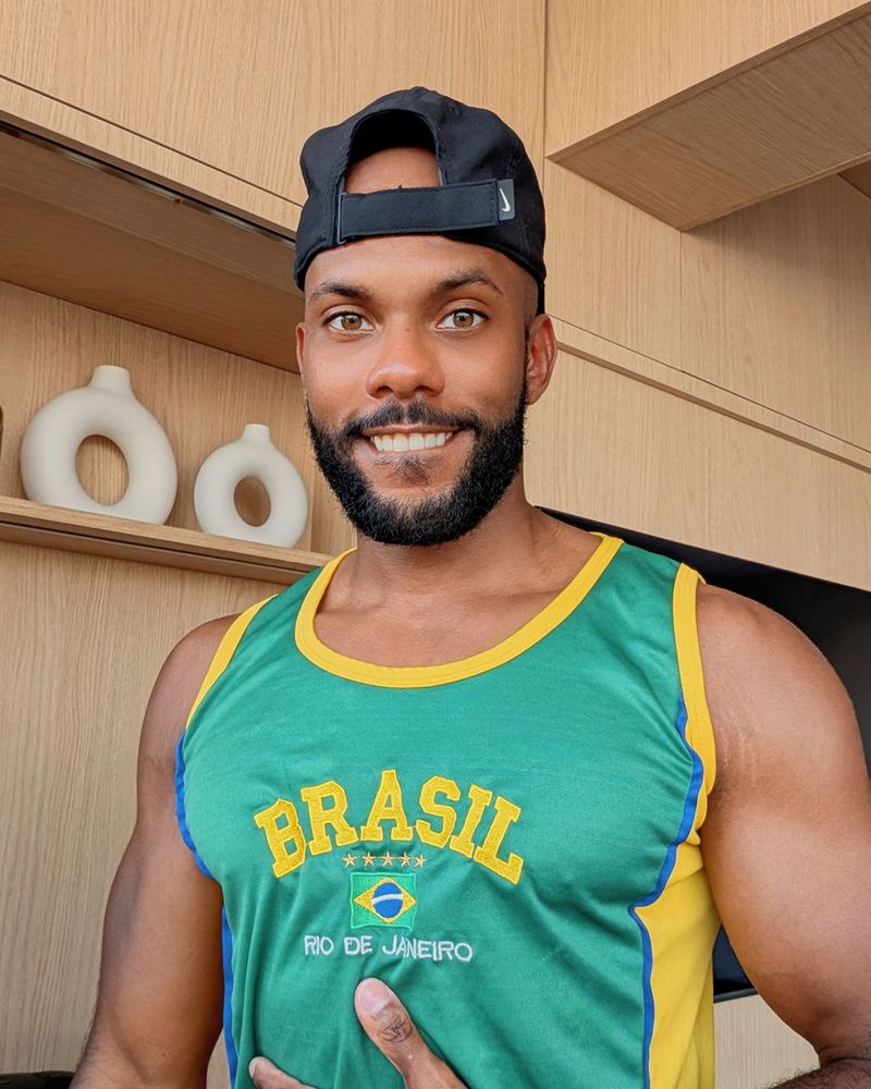 Gay muscle butt bottom with a black beard and mustache, wearing a backward black cap, with green and yellow soccer tank top that says "BRASIL" 