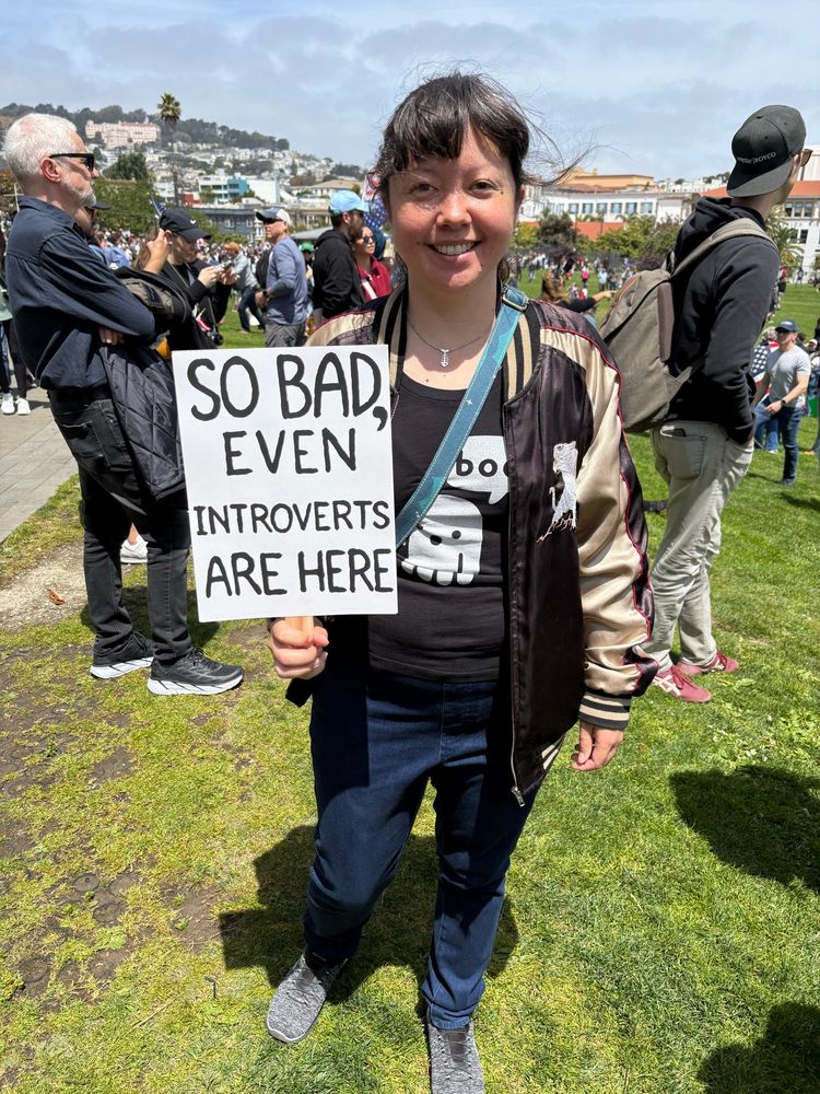 Me holding my sign, which reads “so bad, even introverts are here”.