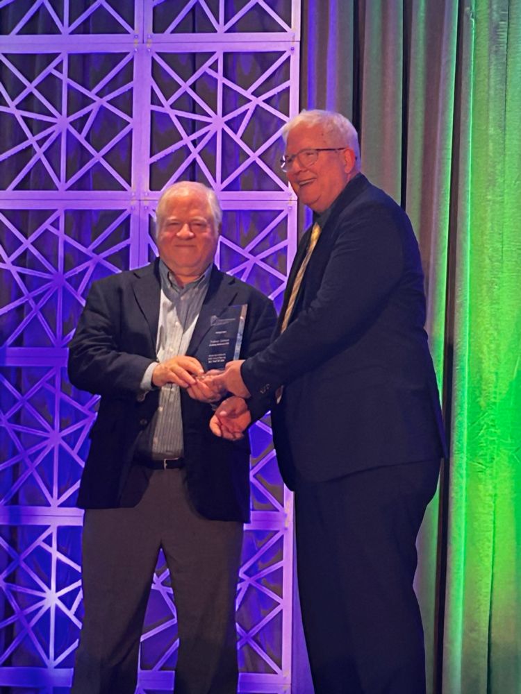 Nelson receives a plaque from Dr Stephan Lewandowsky after the Psychonomics keynote address. The background is lit in purple and green.