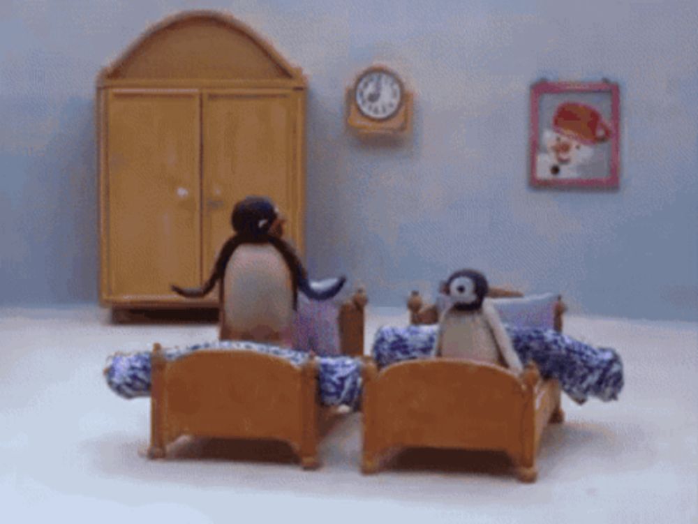 two penguins are sitting on a bed in a room with a clock hanging on the wall