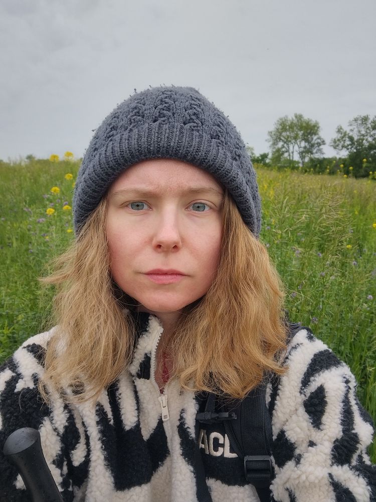 selfie of a blonde animal in a knit hat and fuzzy fleece next to some prairie greens