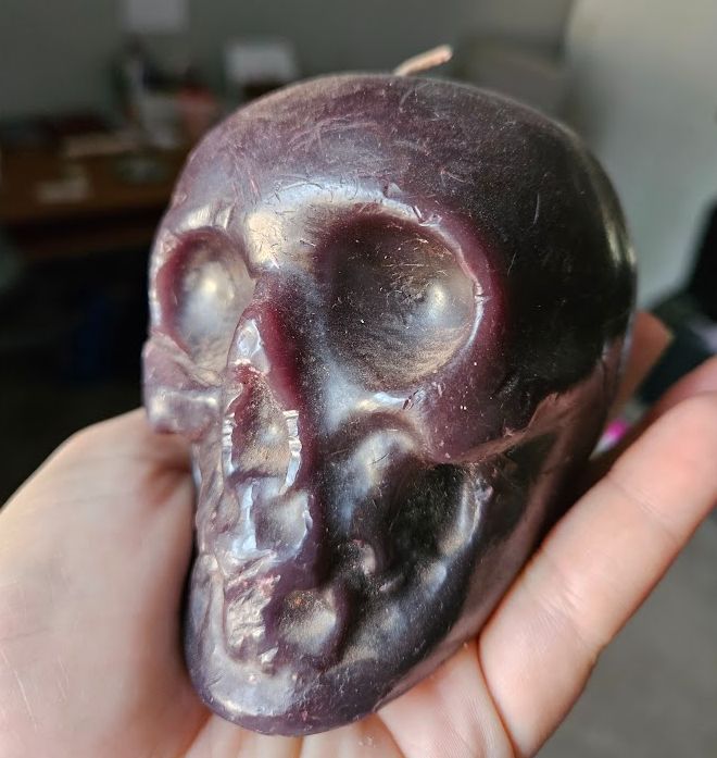 A hand holding a blackish-purple skull candle.