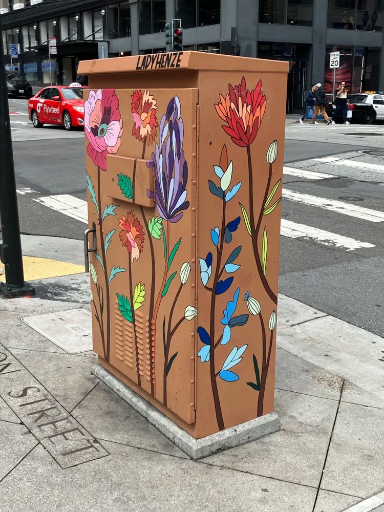 A signal control box has been painted brown with flowers in a way OP is alluding reminds her of taylor swift's piano during the acoustic section of the eras tour. the full showcase of the piece can be found at https://ladyhenzeart.com/#/stockton-and-post-union-square/