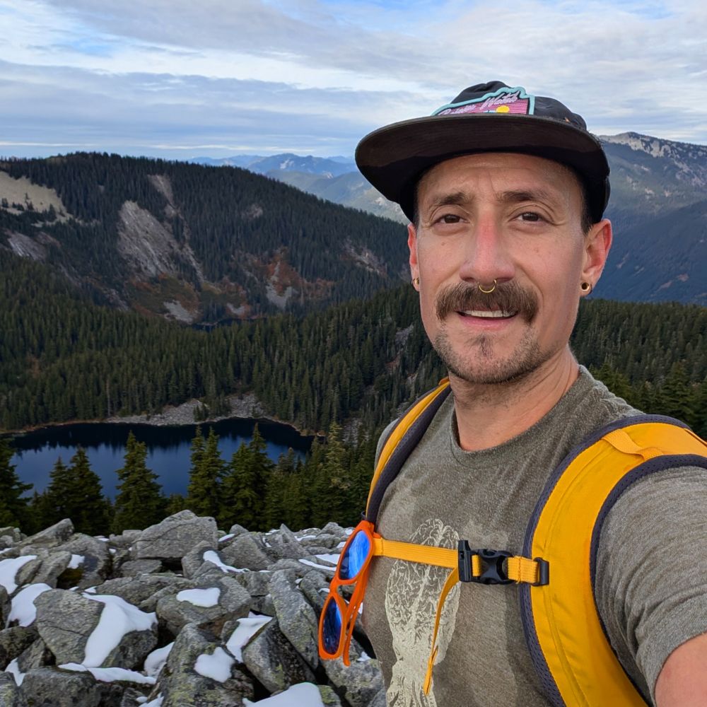 A  selfie from the top of the mountain with an alpine lake in the background 