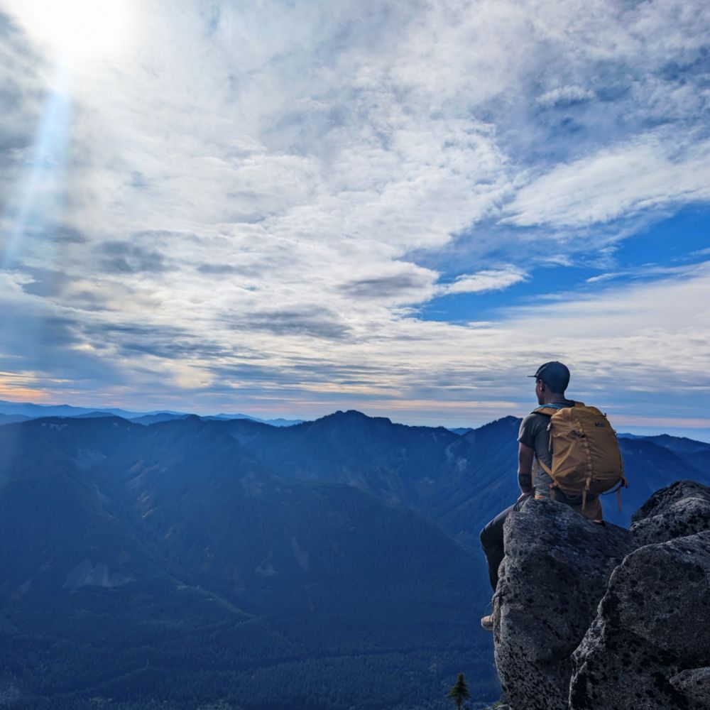 A photo of a person sitting on a rock outcropping looking into the distance 