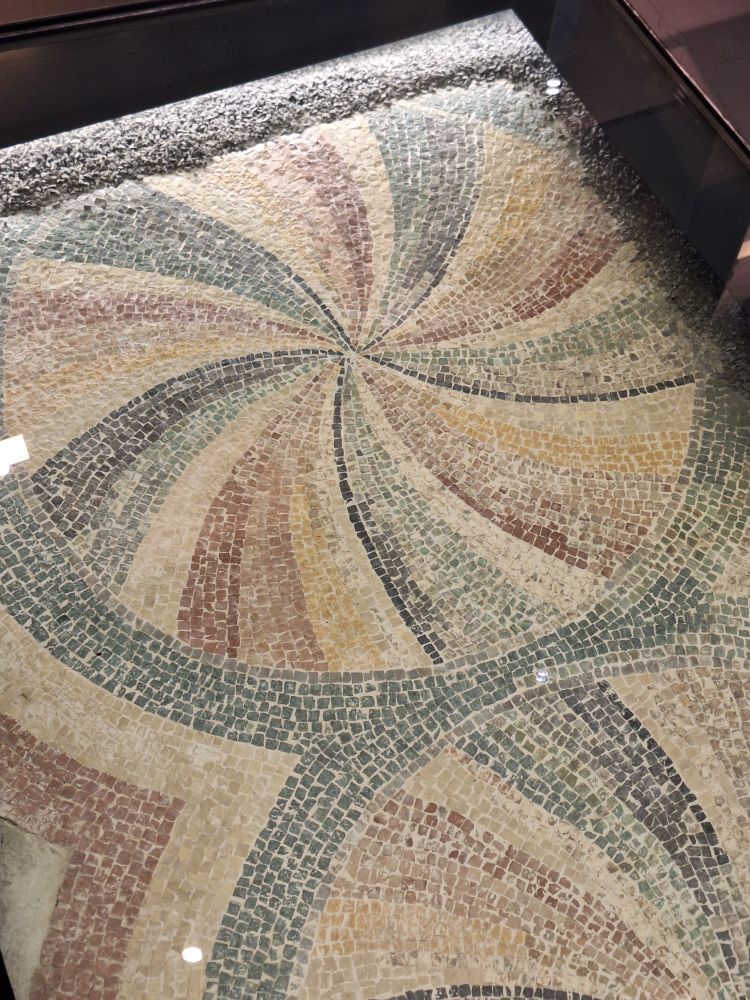 Photo of a mosaic comprised of a large circle with stripes fanning outwards from its center. 