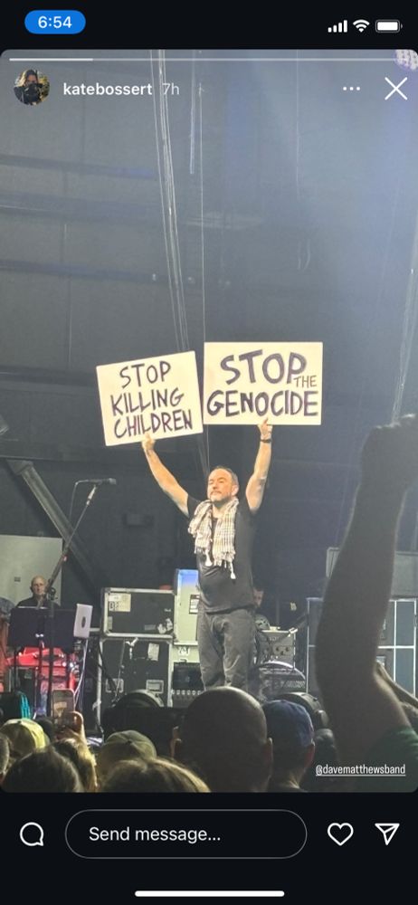 Dave Matthews holding up two signs on stage: Stop killing children and stop genocide 