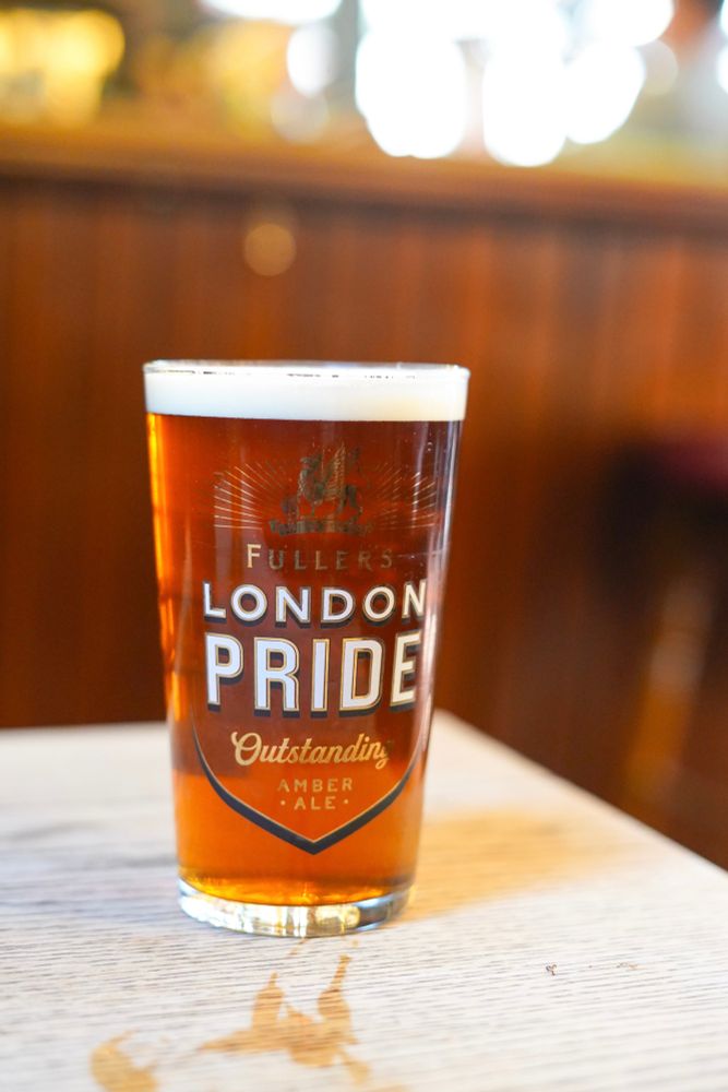 Pint of fuller’s lond pride cask in a branded glass on a wooden table