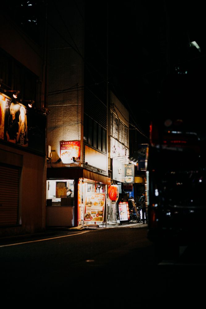 photo of a cozy side street of Tokyo at night, with a restaurant brightly lit with signs and lamps