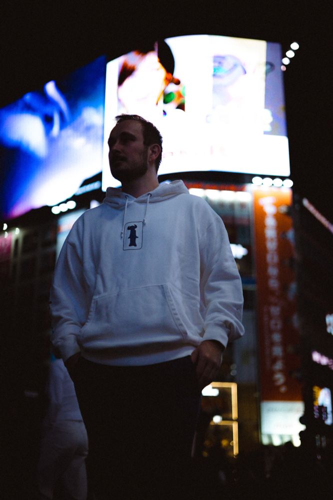 Photo of a person standing at Shibuya crossing, with lots of bright billboards and neon signs in the background.