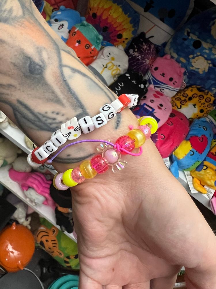 Kandi bracelets.  One has beads that read I.C.I. 🐱 ISG 🍄 FMR 🌼 INTTV 