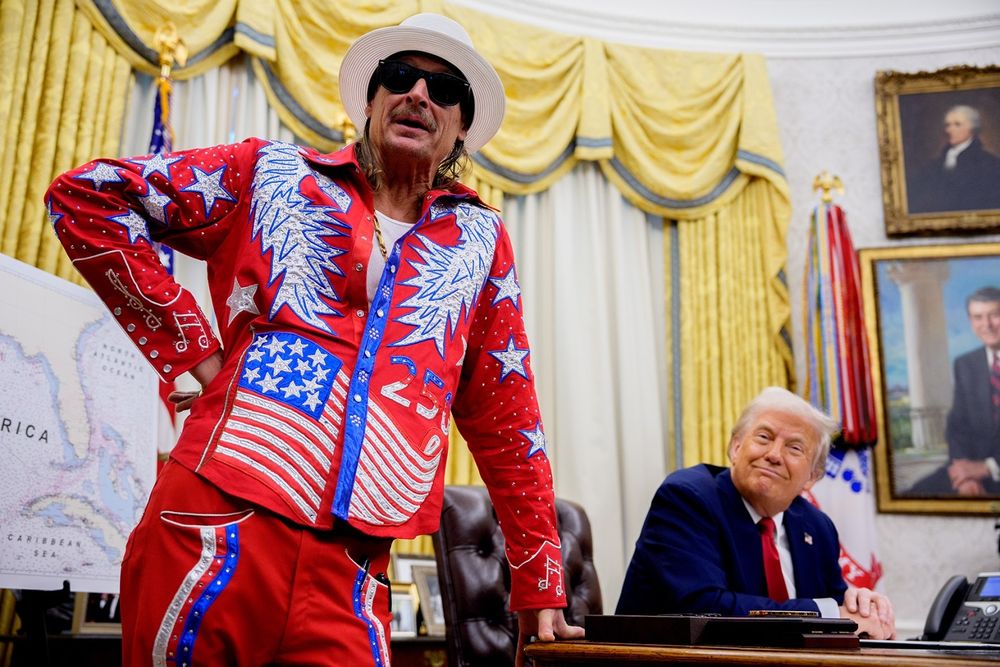 Trump entertains Kid Rock in the Oval Office at the White House. The guest is dressed in a very loud, bright red casual outfit, nothing like a 