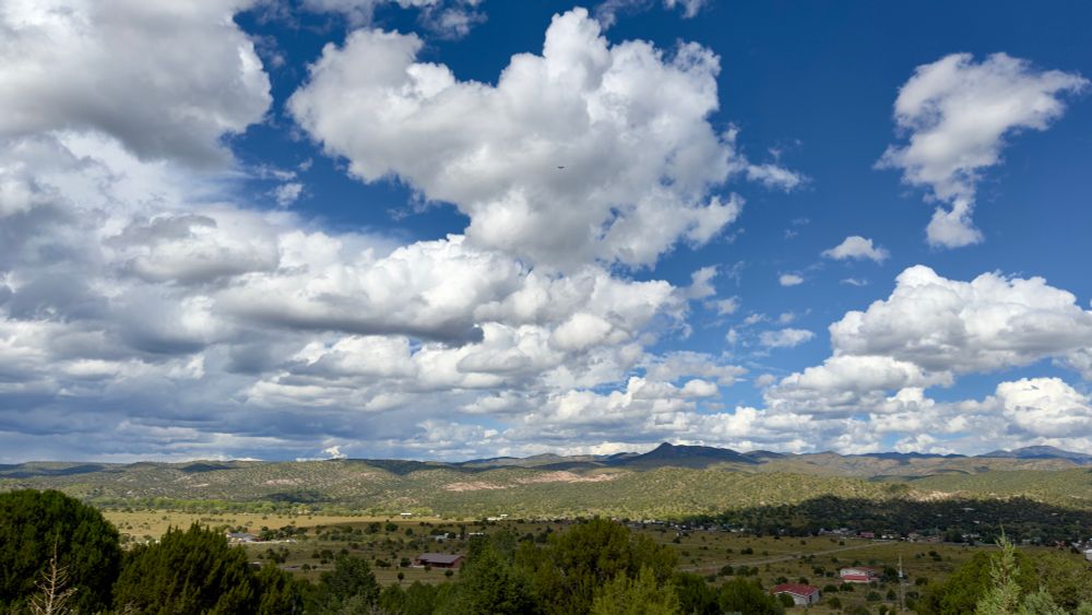 A panoramic view of the members Valley in New Mexico, Land of Enchantment. White puffy clouds, floating in a deep blue sky, hovering above distant mountains and a green high desert valley.