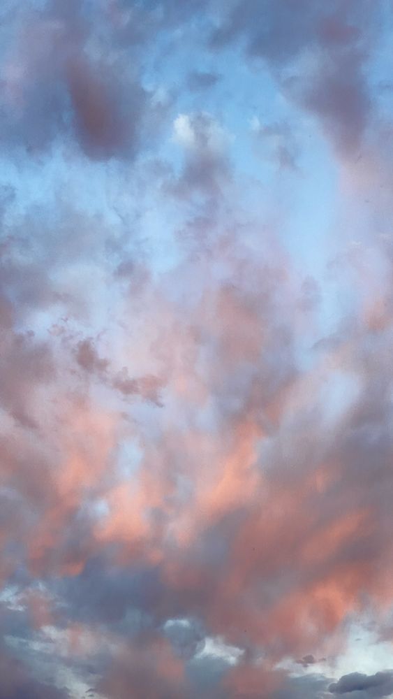 Evening sky scene in Taos, New Mexico with bright orange, pink, and violet colored clouds against a pale blue sky.