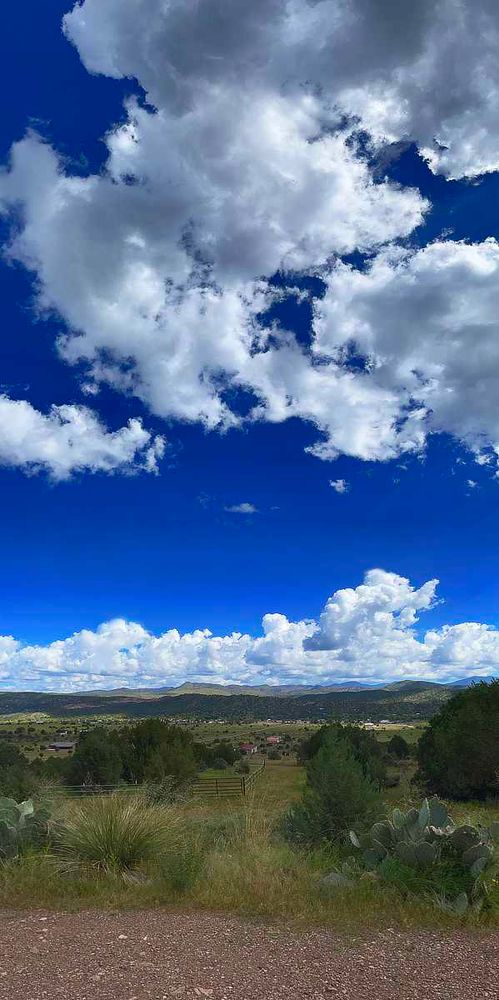 White clouds in a blue sky above a green valley with piñon and cactus in Mimbres, New Mexico.