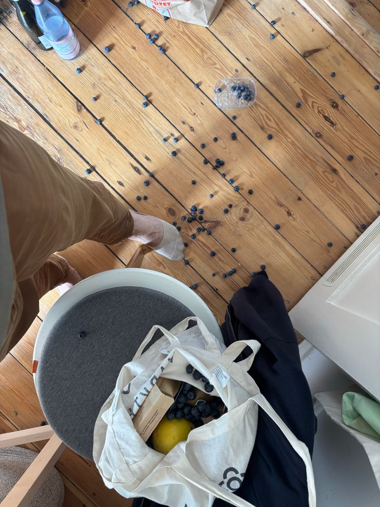 Foto eines Dielenbodens, auf dem Heidelbeeren zerstreut liegen. Daneben Einkaufsbeutel mit anderen Artikeln auf einem Stuhl + meine Beine.