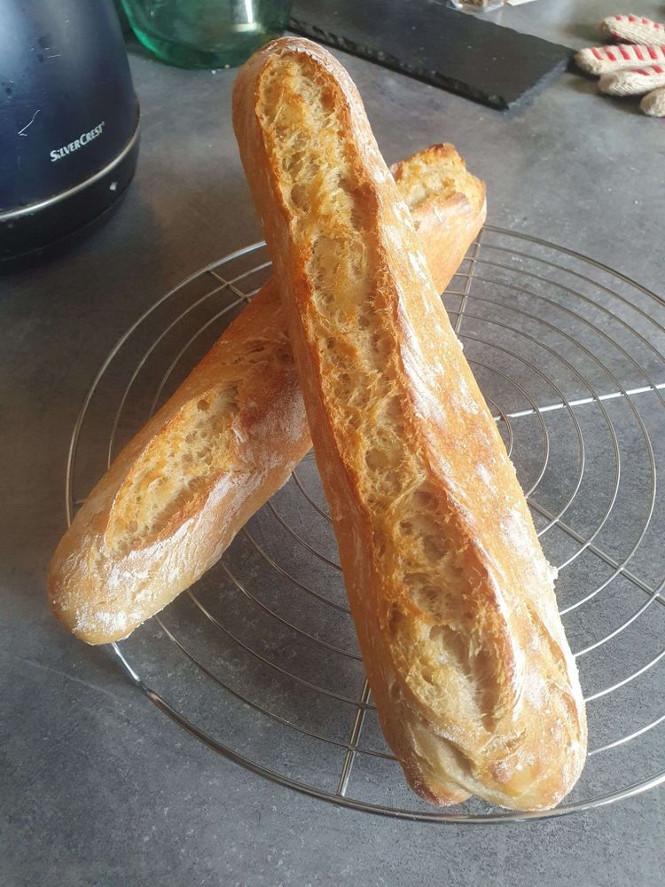 Sur une grille, à refroidir, 2 baguettes superposées, celle du dessous à des grignes latérales, celle du dessus une grigne centrale. Elles sont légèrement farinées.