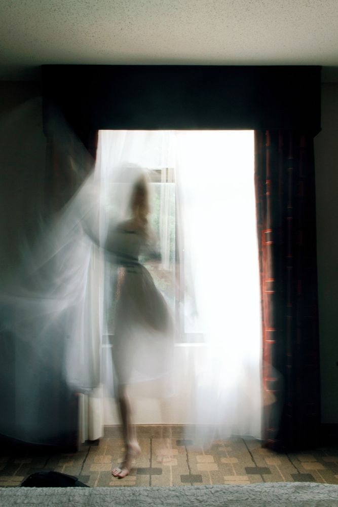 Long exposure of the photographer in a white gown infront of a large window with sheer white curtains, I'm moving in a dance-like way and blurry, it almost looks like I'm a ghost entering through the windows.