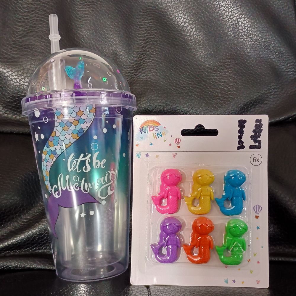 Links ein transparenter Becher mit Kuppel-Deckel und Strohhalm. Auf dem Becher sind ein mehrfarbiger Fischschwanz mit lila Fluke und weiße Blasen auf blau-lila Hintergrund gedruckt, dazu in weißer Schreibschrift "let's be mermaid". Im Deckel steht ein weiterer Fischschwanz.
Rechts ein Blister mit 6 Meerjungfrau-Radiergummis: rosa, gelb, blau, lila, orange, grün