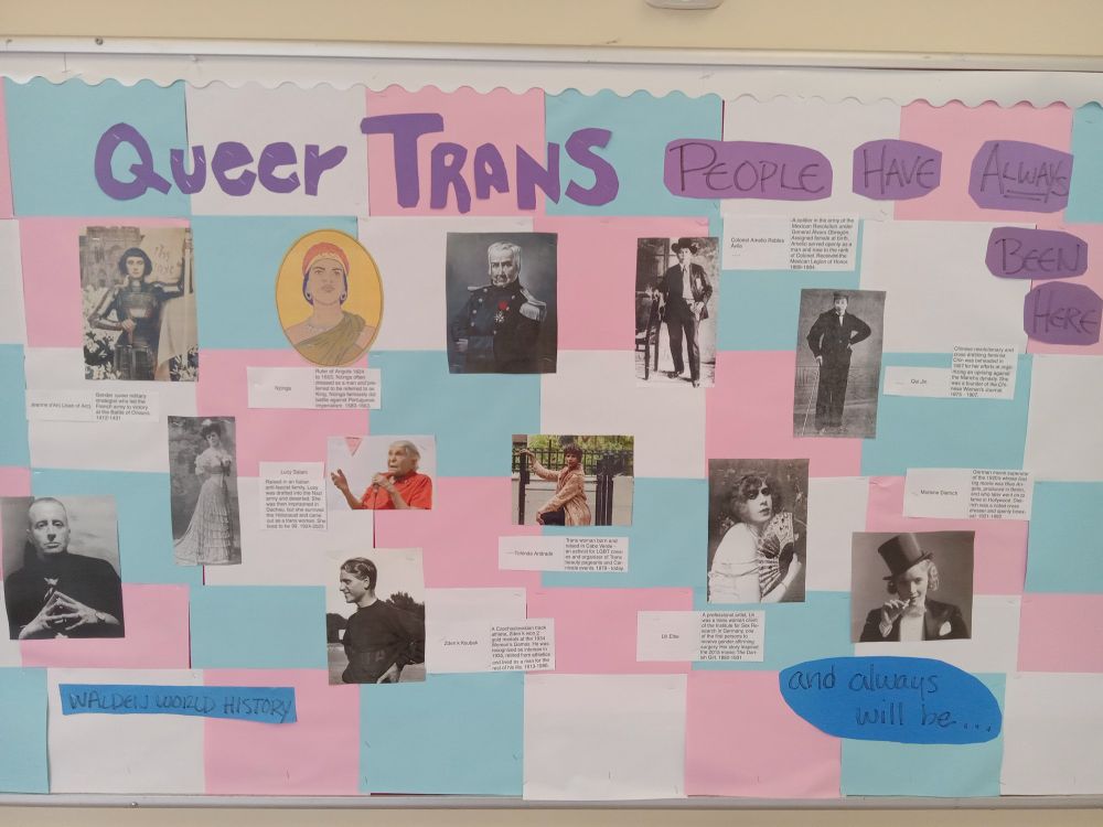 Bulletin board titled "queer trans people have always been here" has pink, light blue and white checkerboard and photos of notable trans people from world history such as Joan of Arc, Qui Jin, and Amelio Robles Avila.