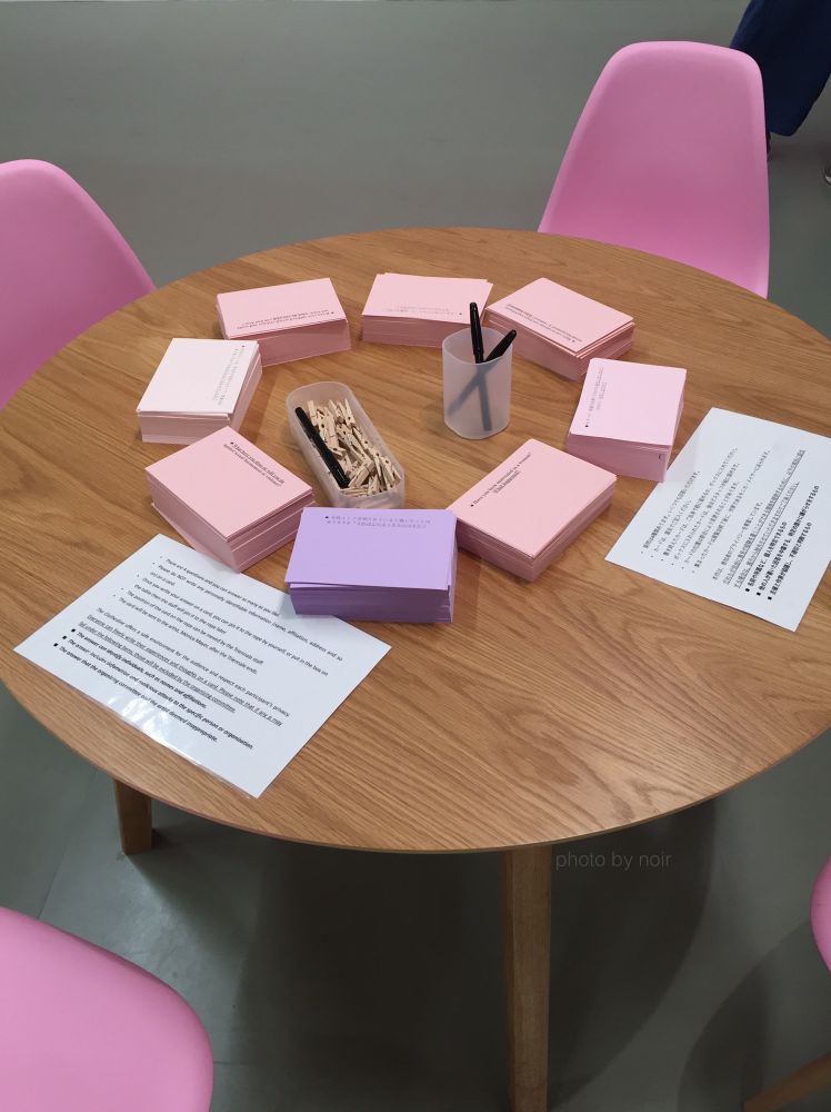 円形のテーブルの上にペンと8種類のカードが並べられ、ピンクの椅子が4脚テーブルの周りに置いてある。カードの書き方の説明書が日本語と英語の2種類置いてある。
薄ピンクから薄紫までピンク系の色で作られたカードには「女性として差別されていると感じたことはありますか? それはどのようなものですか?」などの異なる4つの質問が印字されていて、その下に参加者が回答を書くための余白がある。カードも日本語と英語の2種類ある。