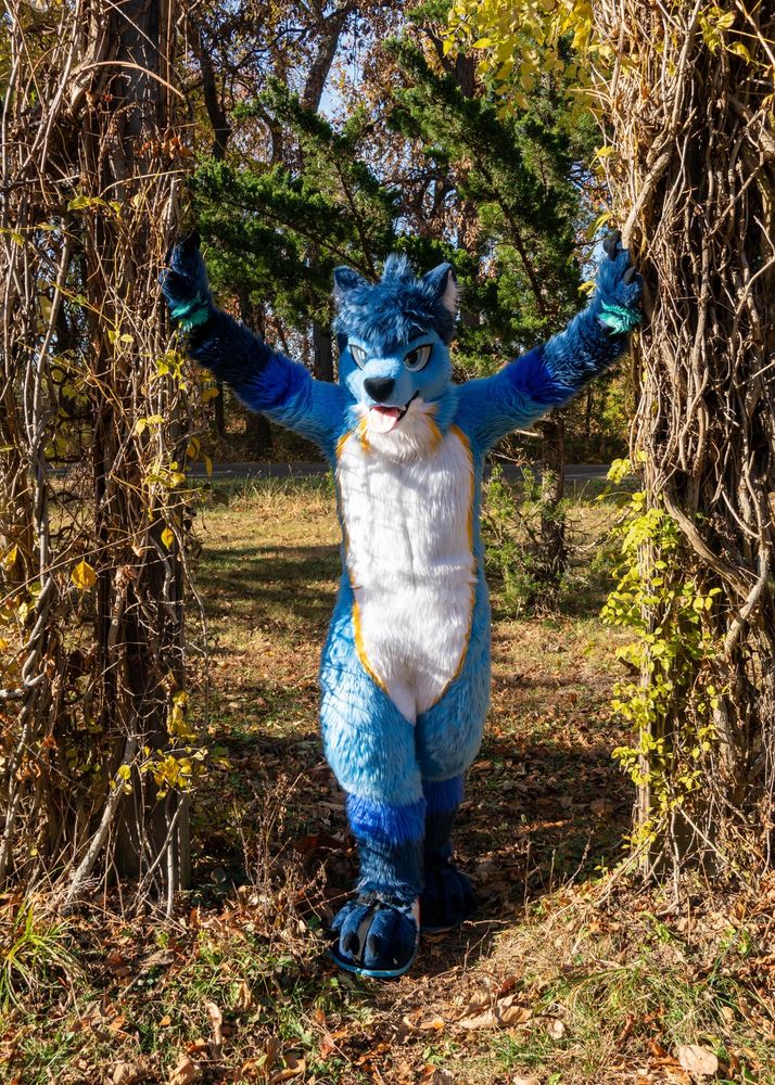 me in my full fursuit, standing in a gap in a wall of vines, with my two hands propping up at the walls, and my right leg in front of my left