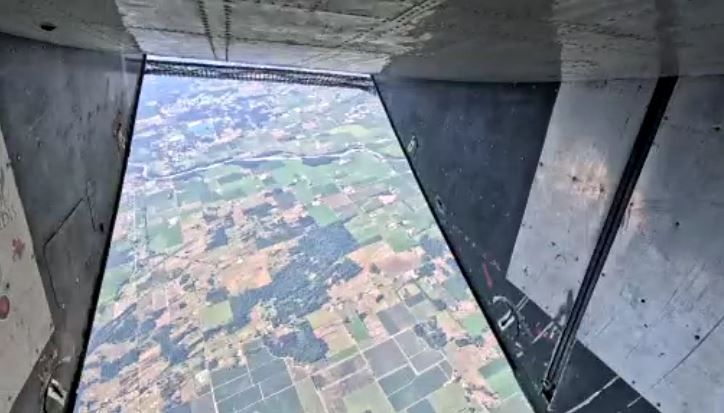 The view out the open door of an aircraft with little squares of farm field below