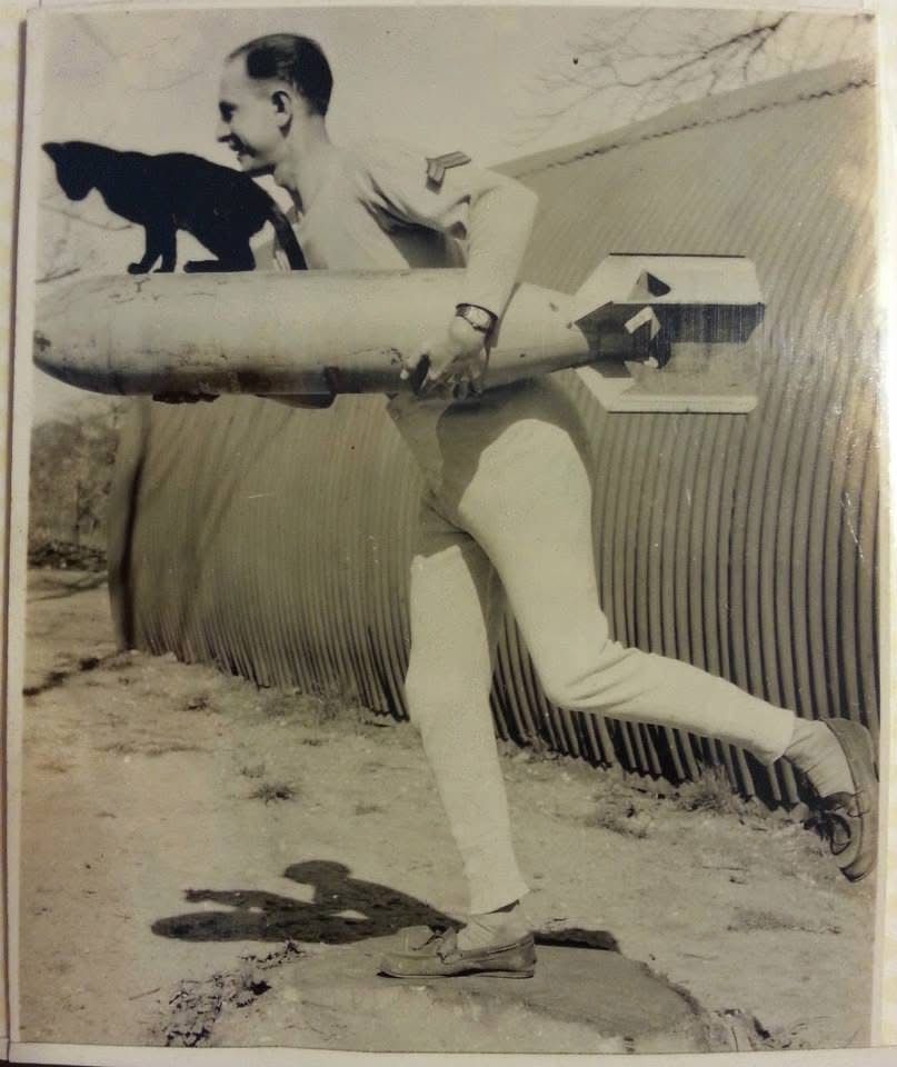 Old picture of a soldier in long johns in a running pose holding a torpedo(?). A black cat sits on top of the torpedo in a pose mirroring the man’s.