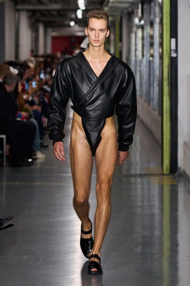 A man in a long-sleeve V-neck bodysuit with shoulder pads and sandals. It doesn't look comfortable. Or warm. Or practical. I bet it isn't cheap either. 