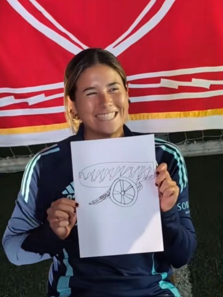 Kyra Cooney-Cross smiling holding a paper with a handrawn arsenal cannon