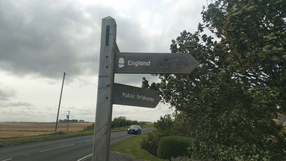 Wooden sign with one pointer labelled 'England' and the one below in a different direction 'Public Bridleway'