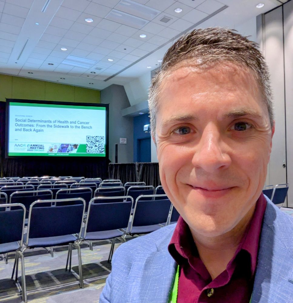 Matt in front of the cover slide reading 'Social determinants of health and cancer outcomes: from the sidewalk to the bench and back again". 