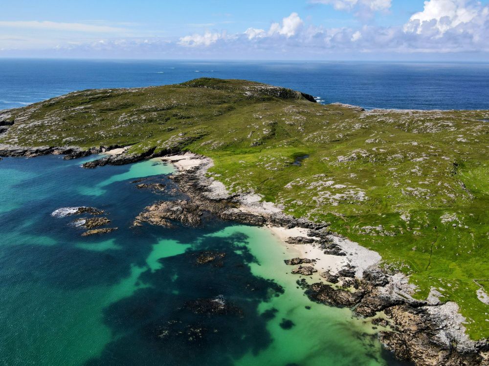 Ariel view over costal headland with white sandy beaches and jade coloured sea