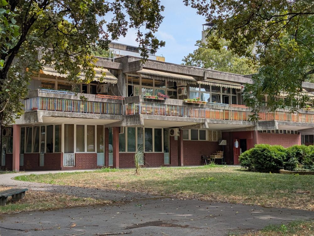 A cozy building in one of the districts of the New Belgrade. Built around 70th, I guess. Even made in the brutalism style with all decor elements made from the raw concrete it does not look dark, because of the amount of green around. For me it fits into the surrounding very well.