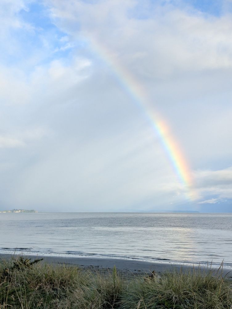 A view from coastline out to sea, where a half-rainbow is present.
