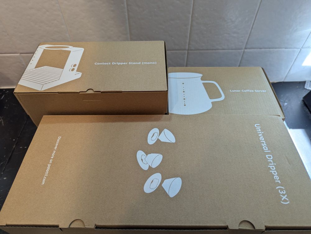 A set of boxes holding a metal stand, ceramic carafe and 3 finely crafted ceramic filter holders.