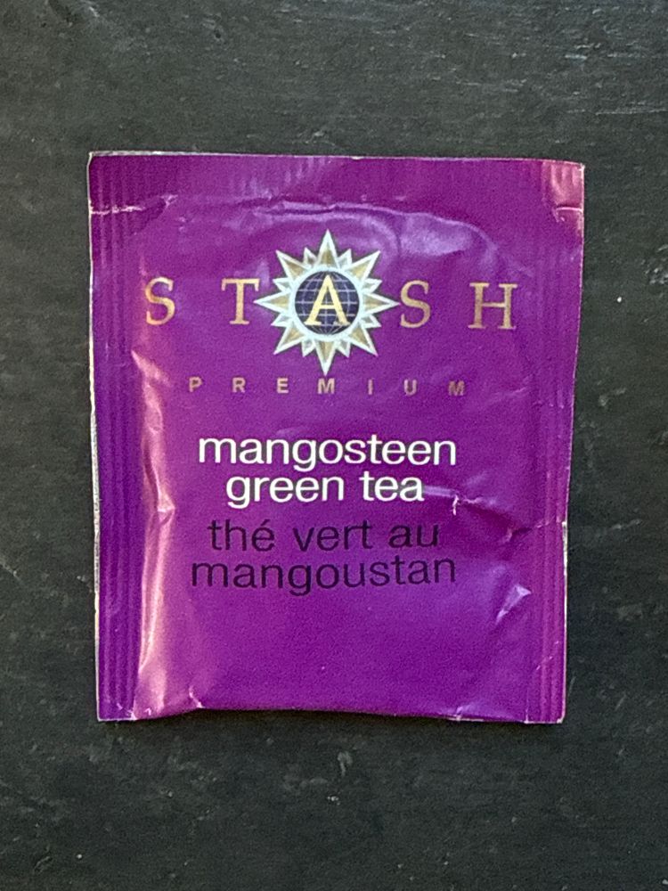 Closeup photo of a packet of Stash premium mangosteen green tea. It is a medium purple color with white, gold, and black writing on it.