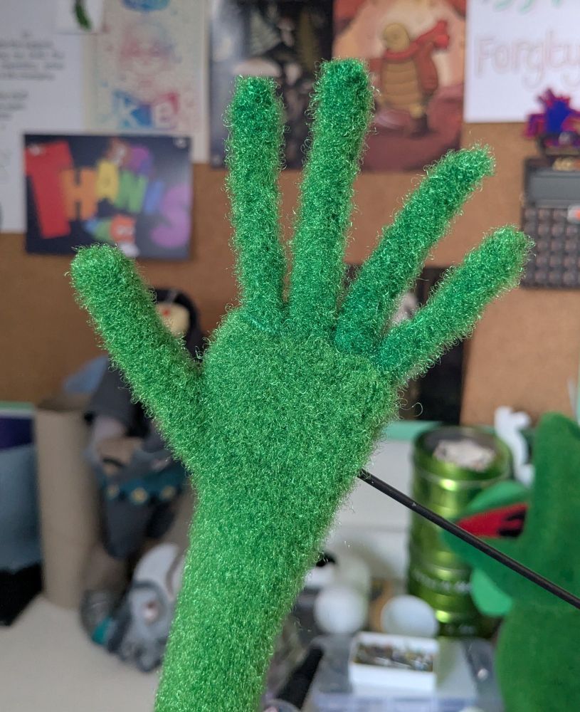 A fuzzy green Kermit hand, waving hello.