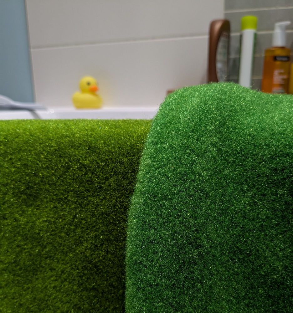 Two sheets of green fleece fabric drying over the side of a bathtub. They're completely different shades - the one on the left is a nice, yellowy mossy green, while the right one is more blue looking. 
