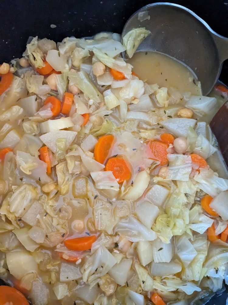 Pictured is a hearty soup in a pot with cabbage, chickpeas, carrots and other root vegetables.