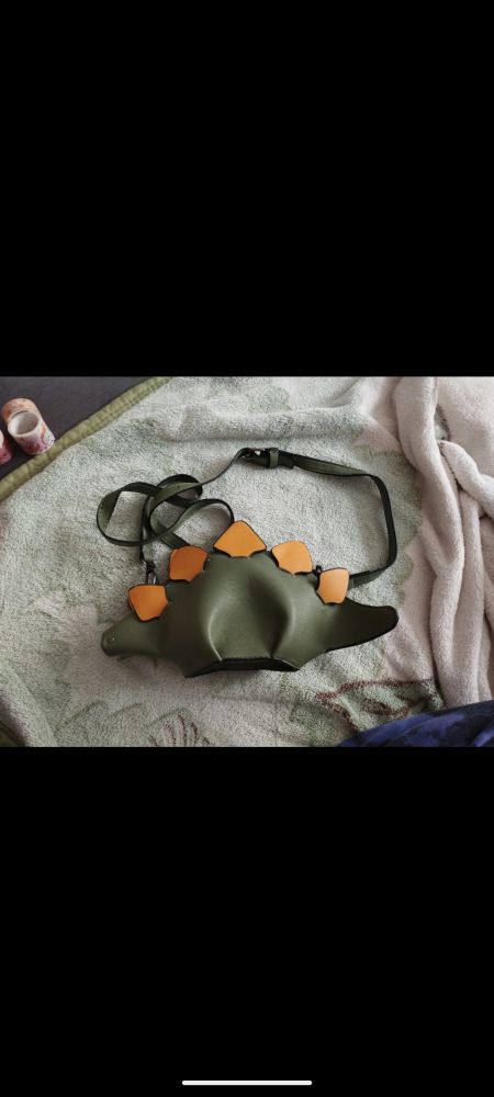 Foto von einer grünen Tasche in Stegosaurusform mit gelben Zacken. 