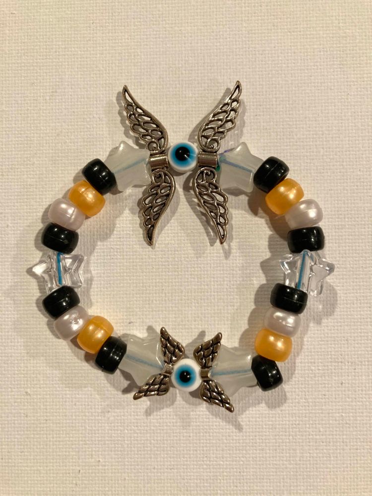 bracelet made of pony beads. theres black, gold, and silver beads along with transparent stars. there are also two places with eye beads that have metal wing beads on either side of them. one has larger wings, the other has smaller ones.