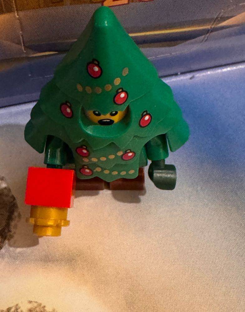 A alarmed looking minifigure holding a red gift dressed as a Christmas tree. 