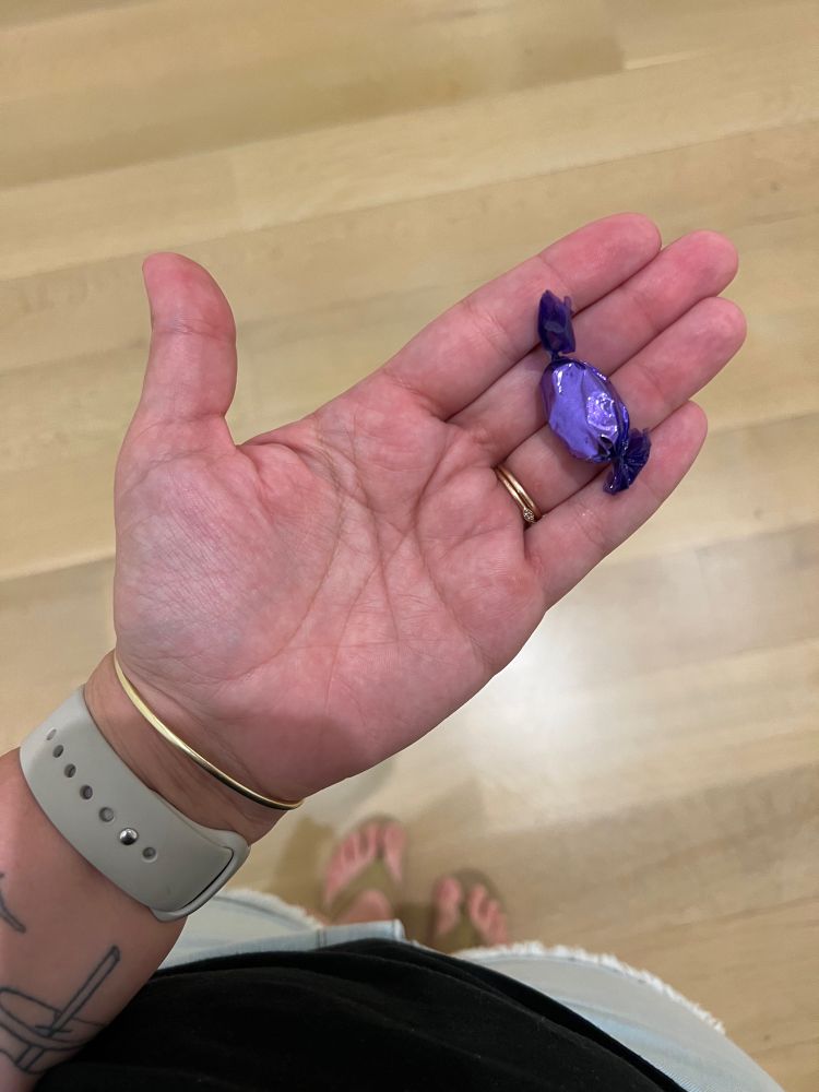 Crystal’s hand holds a purple wrapped candy. 