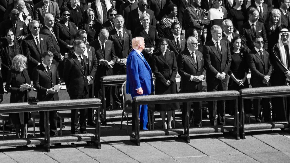 In this photo, taken during the funeral of the Pope, a solemn crowd dressed entirely in black stands in respectful silence. In stark contrast, Donald Trump stands prominently at the center, wearing a glaringly bright blue suit, shattering the unity and solemnity of the scene. His posture and detached expression amplify the sense of isolation and profound disrespect, making him look more like a misplaced spectacle than a statesman, dragging a moment of historic mourning into the realm of global embarrassment.