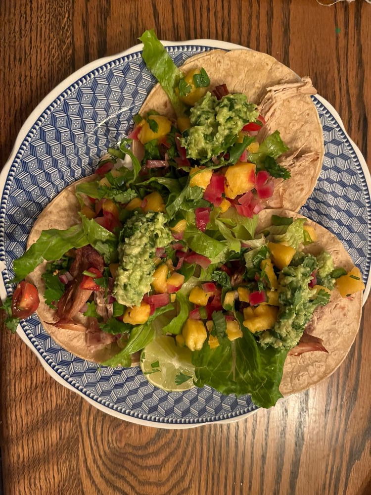 A colorful plate of pork tacos on corn tortillas, with guacamole, pineapple salsa, and pico de gallo.