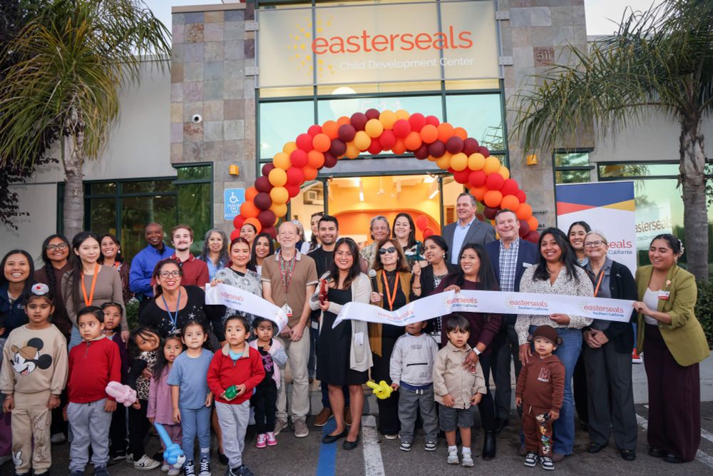 A group of adults and children gathered in front of the Easterseals Child Development Center, standing under an arch of orange balloons. 
